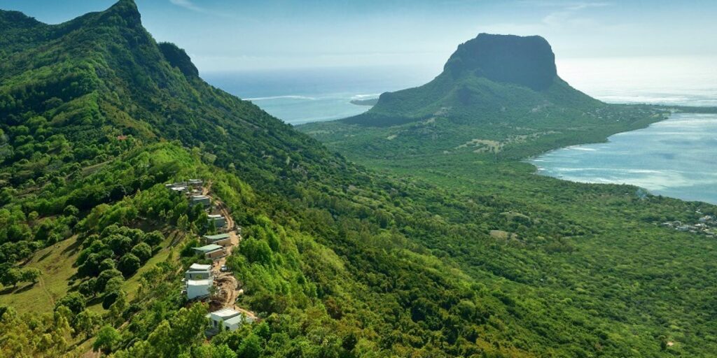 green mountains in Mauritius with houses upon a hillside close up and ocean in the distance