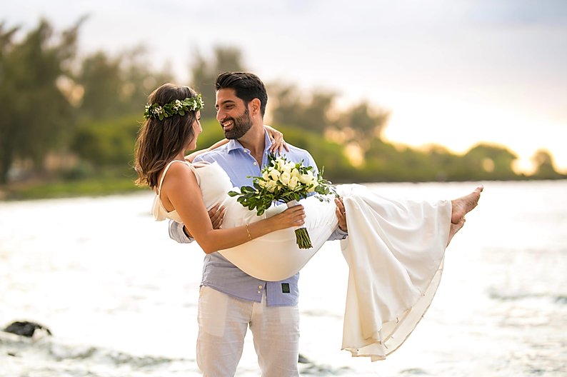 man carrying bride in front of ocean