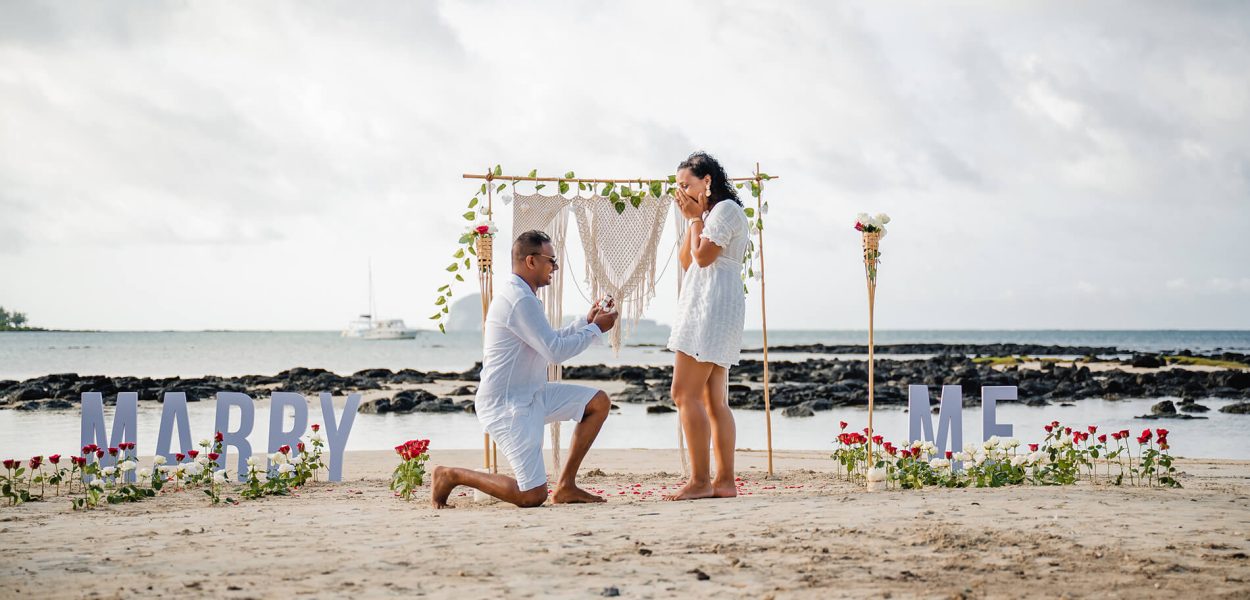 man on one knee on beach asking his partner to marry him