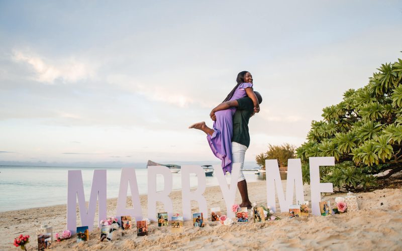 man holding woman after proposing on the beach